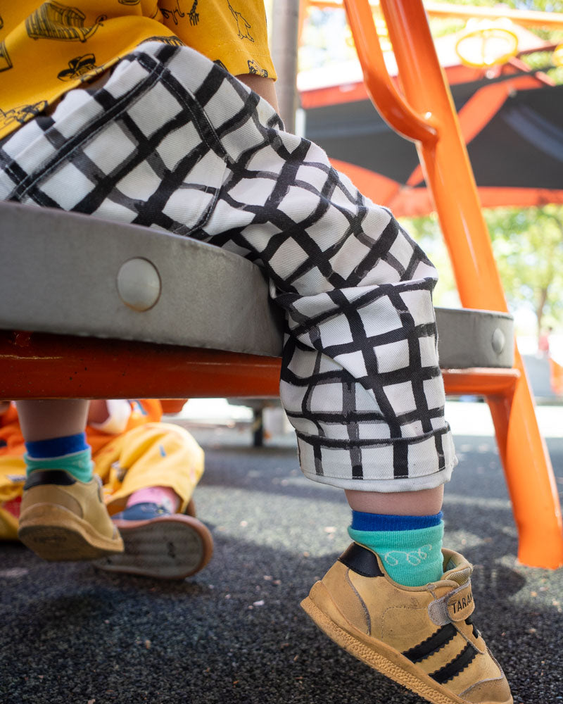 Child's legs wearing checkered pants and blue socks on a playground.