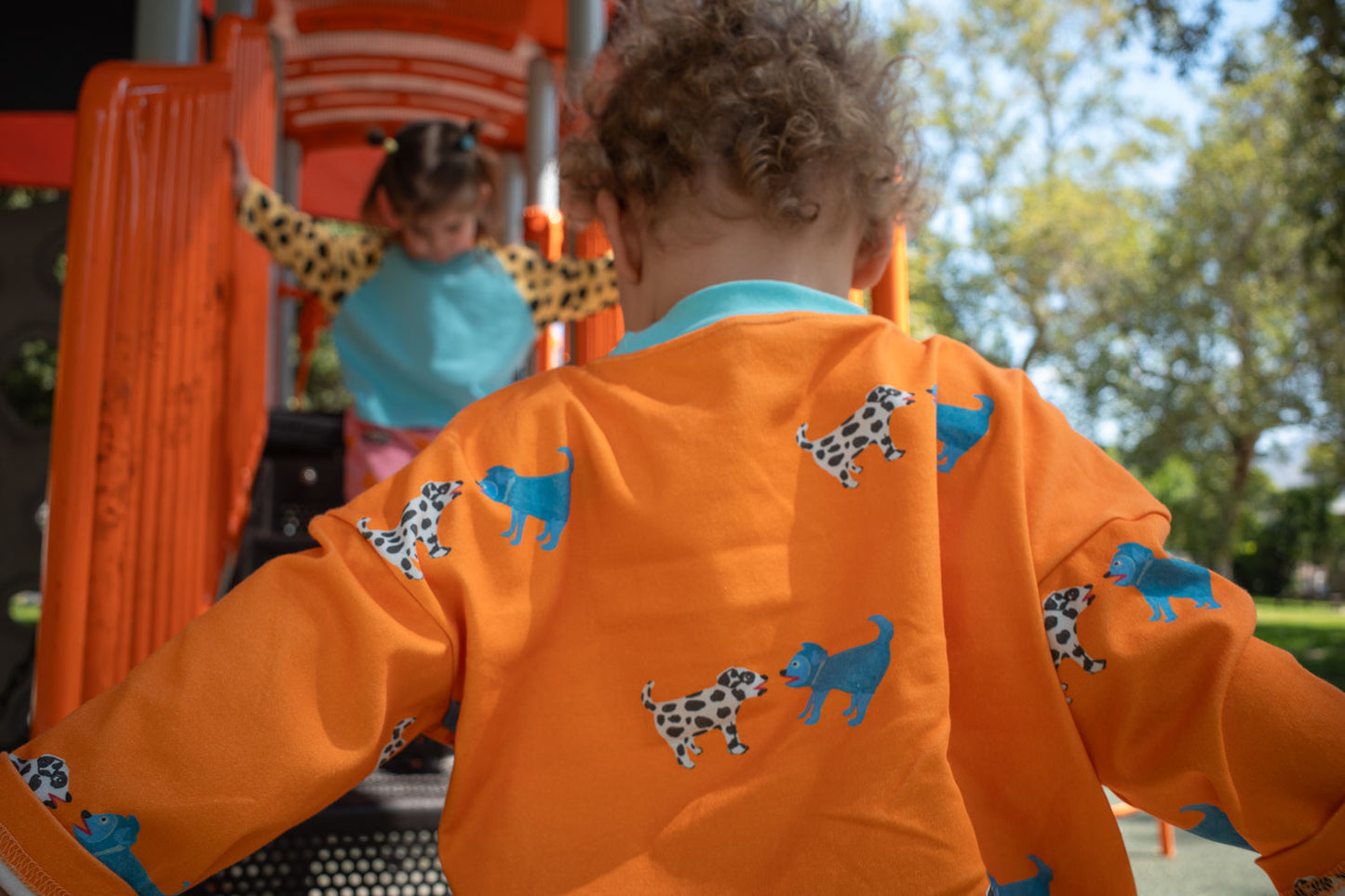 Child wearing an orange t-shirt with dog patterns on a playground