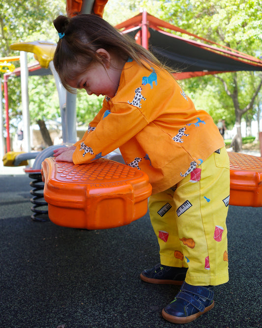 Child playing on a playground wearing yellow printed instrument pants