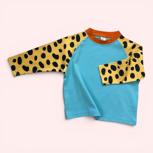 Children's shirt with blue body and yellow sleeves with black spots on a light pink background