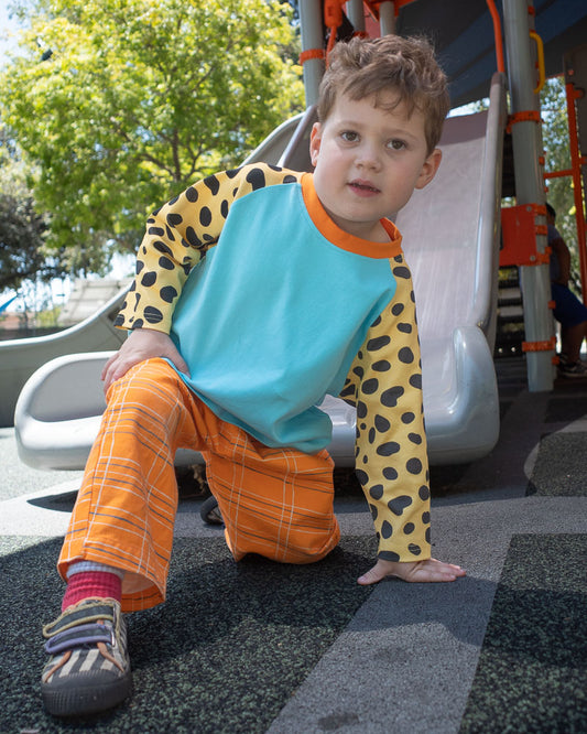 Child in blue raglan t-shirt with black and yellow spotted sleeves sitting on a playground slide