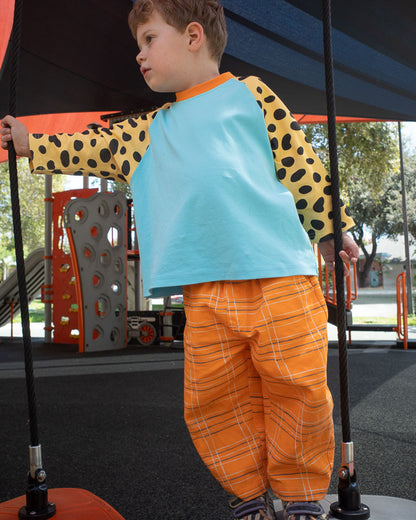 Child in a playground wearing a blue shirt with spot print sleeves and orange plaid pants.