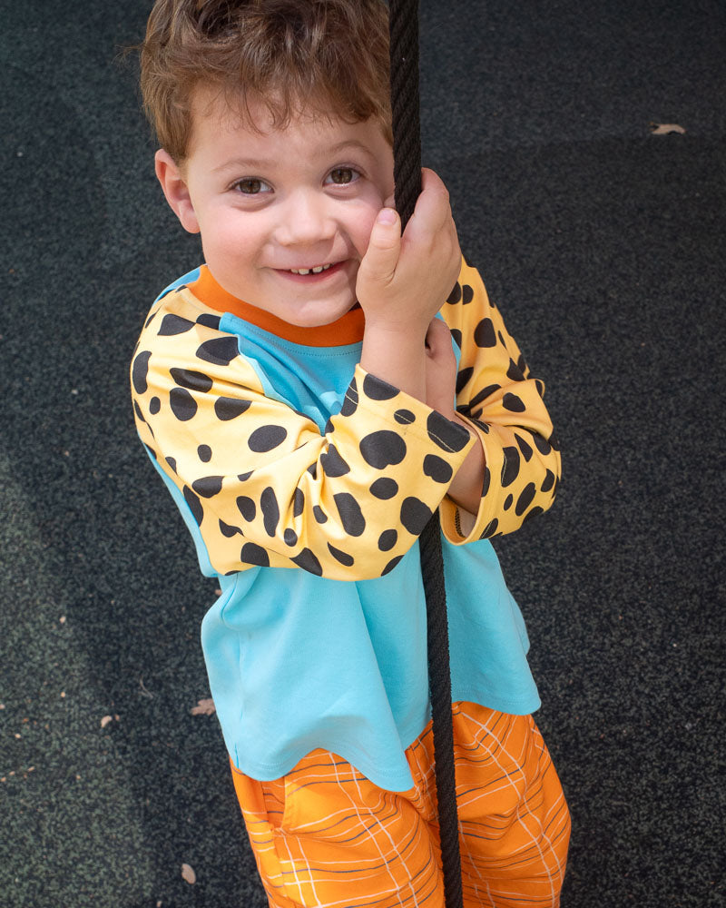 Child wearing a colorful shirt with animal print sleeves and orange pants on a dark surface.