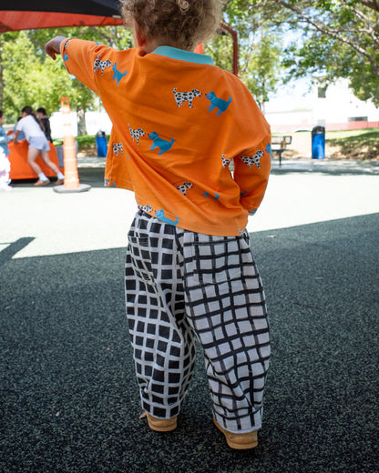 Child wearing an orange shirt with dog patterns and checkered pants on a playground.