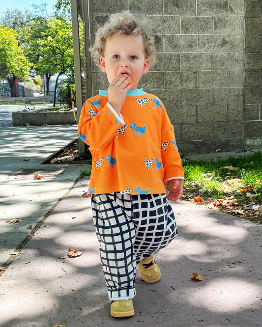 Child wearing an orange shirt with a dog print and black and white checkered pants, standing on a sidewalk.