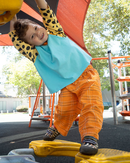 Child playing on a playground wearing orange plaid pants