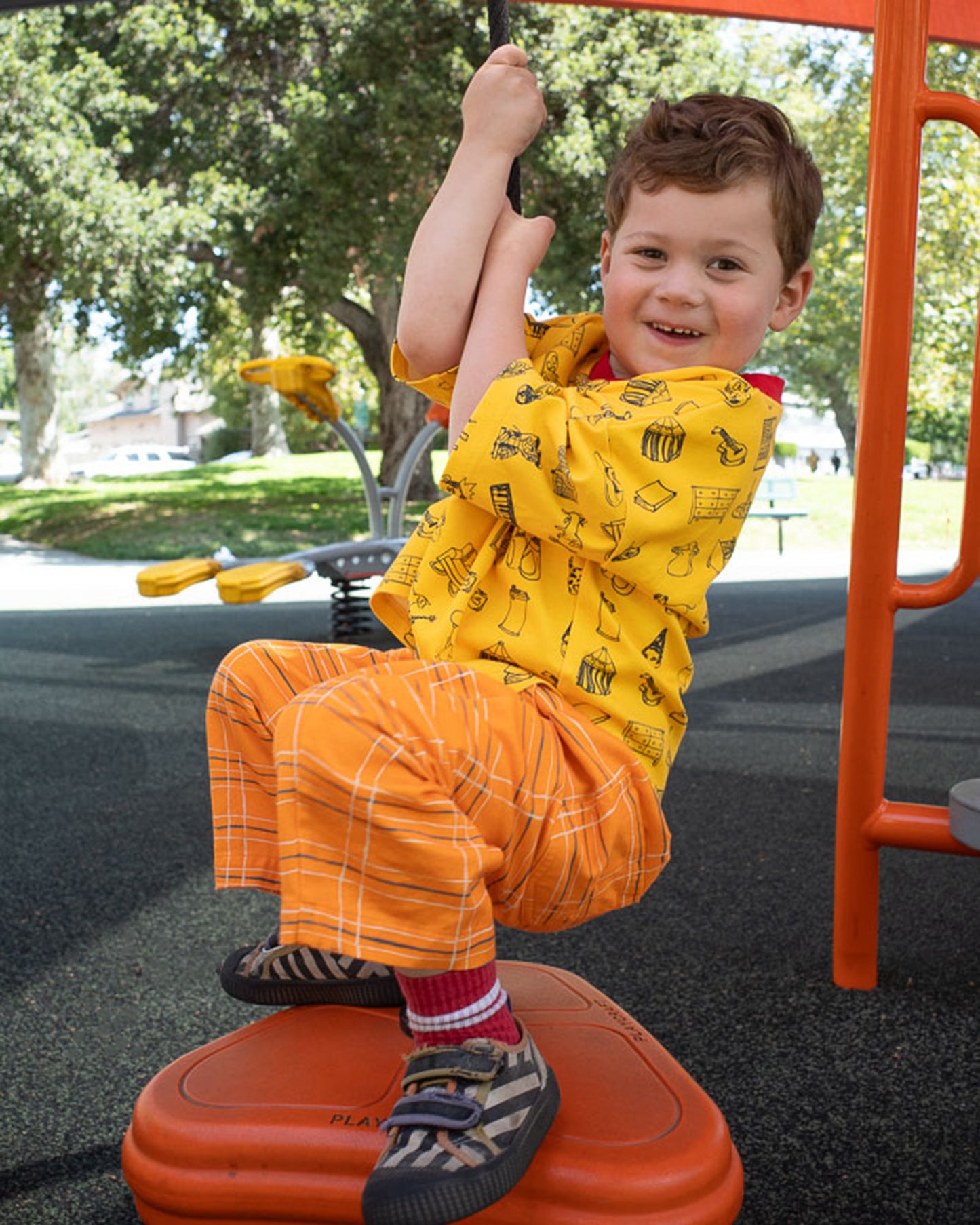 Child playing on a playground structure wearing orange plaid pants