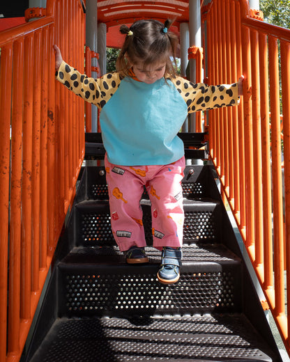 Child in pink printed instrument pants standing on a playground structure with orange railings and black steps.