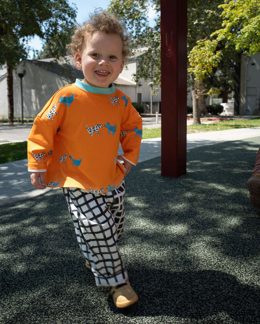 Child wearing an orange shirt with dog print and black and white checkered pants outdoors.