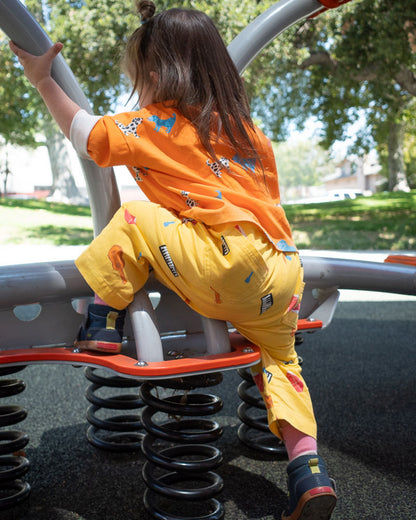 Child playing on a playground structure wearing yellow printed instrument pants