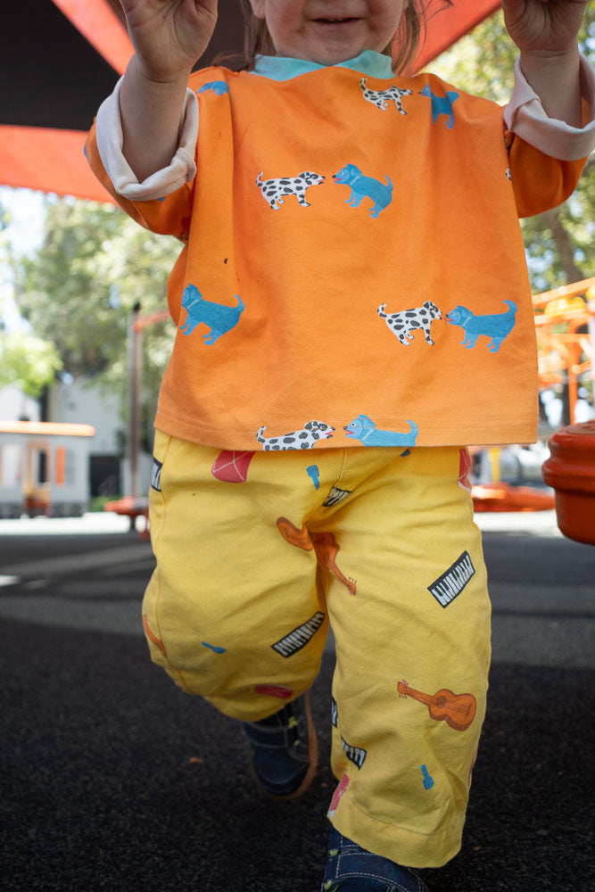 Child wearing an orange t-shirt with dog print and yellow printed instrument pants