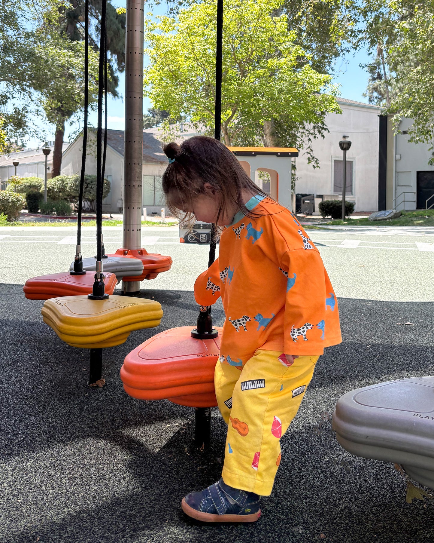 Child playing on a playground wearing yellow printed instrument pants