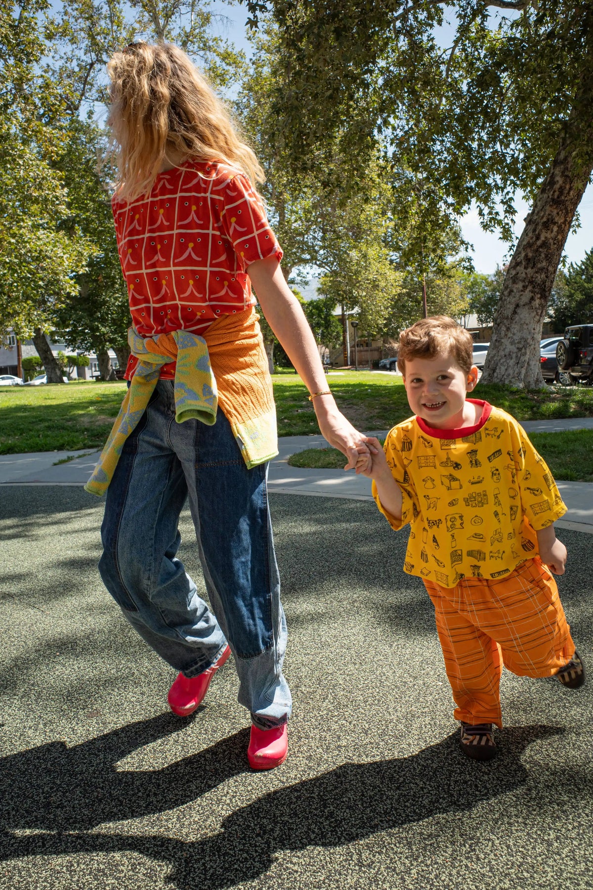 Woman and child holding hands on a sidewalk with trees in the background